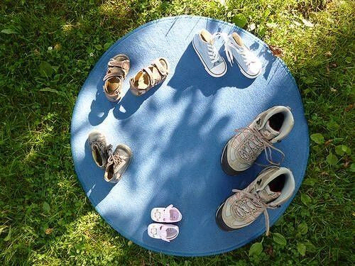 Verschiedene Schuhe auf einer blauen runden Matte im Gras.