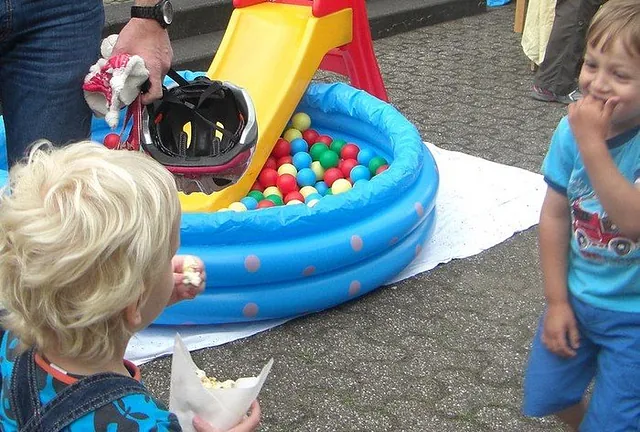 Kinder spielen in einem aufblasbaren Bällebad mit kleiner gelber Rutsche.