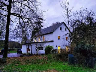 Ein weißes Haus mit erleuchteten Fenstern in einer winterlichen Landschaft.